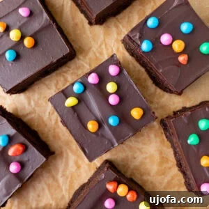 Gluten-Free Cosmic Brownies: Little Debbie Copycat Recipe 3 Overhead shot of gluten-free cosmic brownie squares topped with chocolate ganache and rainbow candy chips scattered on parchment paper.