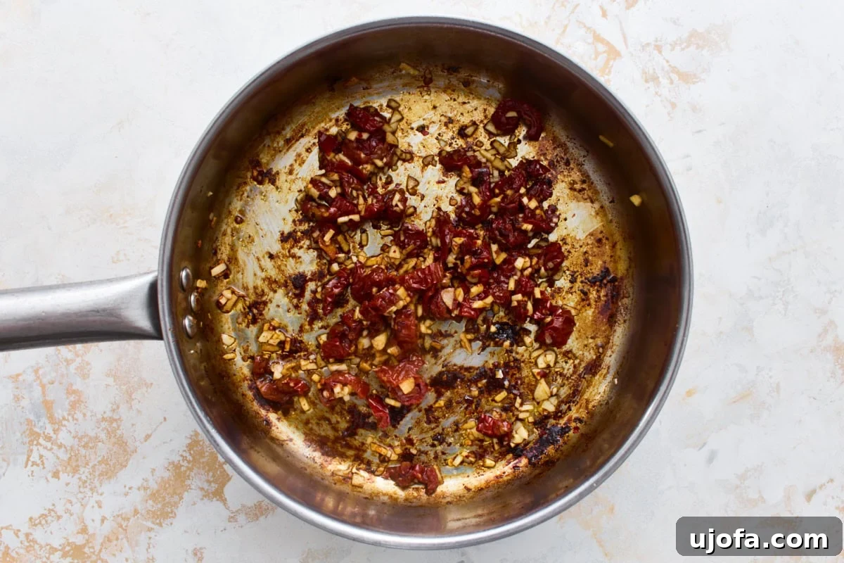 Dairy-Free Marry Me Chicken with Sun-Dried Tomato Sauce 7 Minced garlic and chopped sun-dried tomatoes cooking in a skillet, the flavor base for dairy-free Marry Me Chicken sauce.