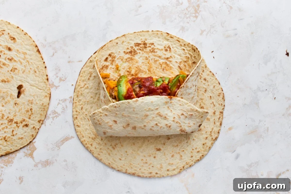 Make-Ahead Gluten-Free Breakfast Burritos 8 Gluten-free tortilla folded over breakfast burrito filling, showing how to roll it tightly