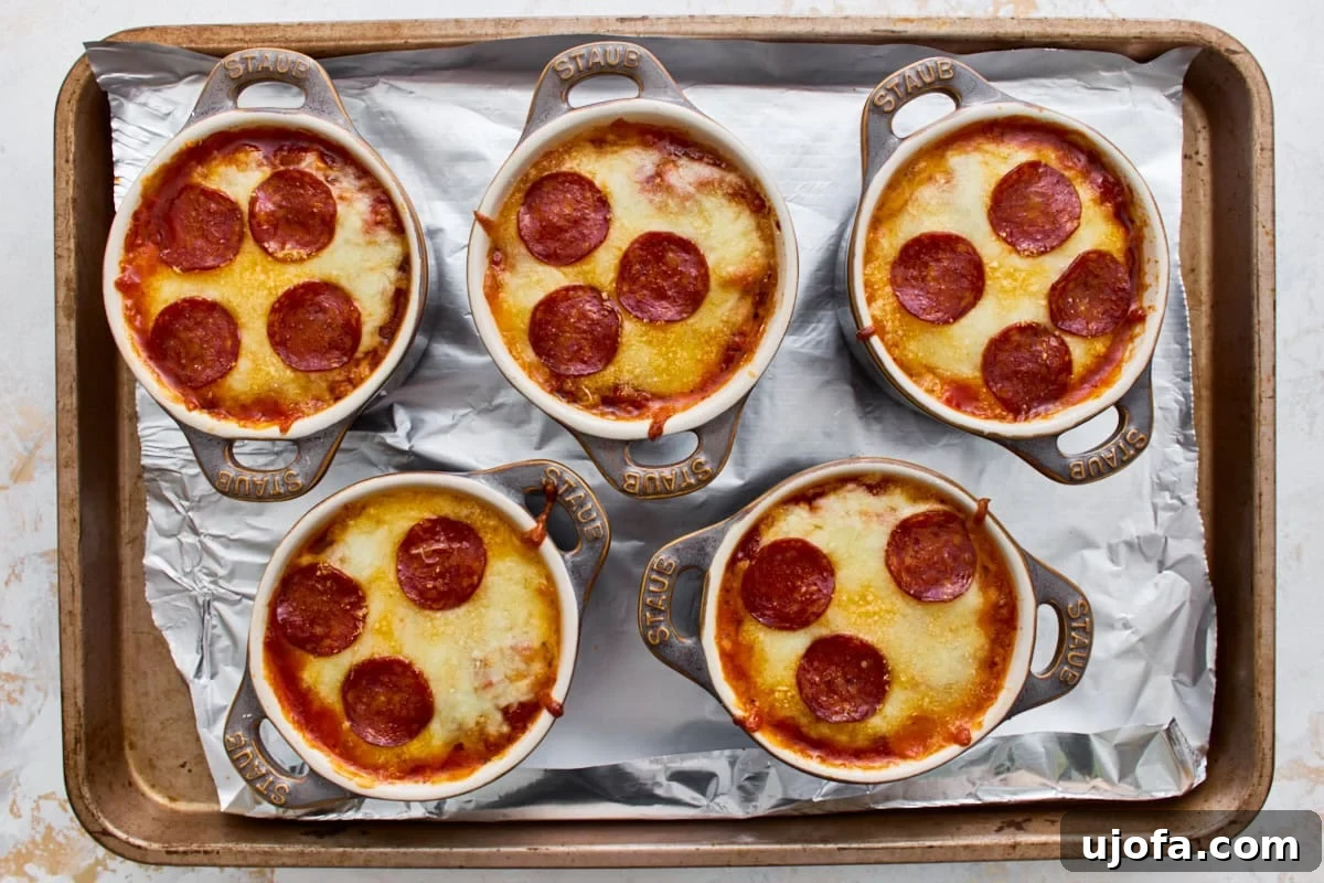 Crustless Pizza Bowl Recipe: Cheesy Pepperoni and Marinara 9 Five gluten-free crustless pizza bowls with melted, bubbly cheese on a baking sheet.
