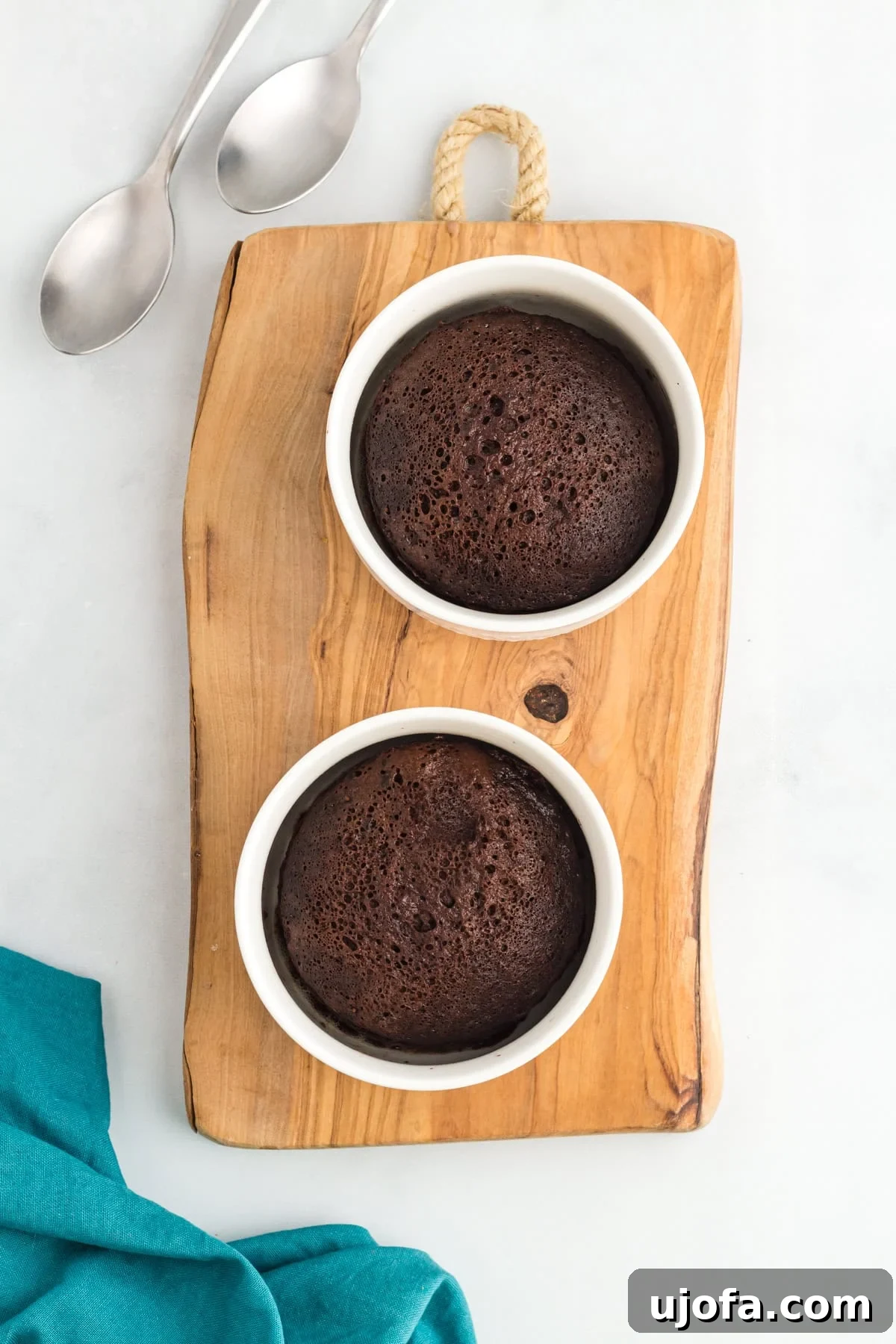 Microwave Flourless Chocolate Mug Cake 2 Two flourless mug cakes baked in white ramekins on a wooden board with spoons and a teal napkin